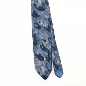 Könnte beinhalten: Eine Krawatte mit dunkelblauer Grundfarbe und einem sich wiederholenden Muster aus hellblauen und beigen, abstrakten, wolkenartigen Formen. Das Design besteht aus komplizierten, fein linierten Texturen innerhalb jeder einzelnen Form.