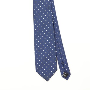 Puede incluir: Una corbata azul con un patrón repetitivo de pequeños puntos blancos. La corbata tiene un extremo puntiagudo y una etiqueta de tela negra visible en la parte posterior con el texto "HANDMADE IN CHINA" impreso en letras mayúsculas blancas.