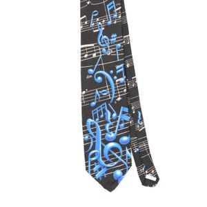 May include: A black necktie featuring a white musical staff pattern with various blue musical notes, symbols, and the text 'cresc.' and 'dim.' printed across the fabric. The design includes treble clefs, sharp signs, and beams of notes.