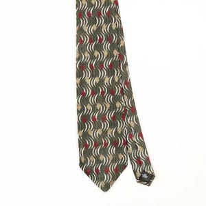 Puede incluir: Una corbata con un patrón repetitivo de líneas onduladas en verde oliva oscuro, intercaladas con pequeñas formas de diamante rojas y detalles geométricos blancos con bordes amarillos. La etiqueta negra trasera indica 100% POLYESTER.
