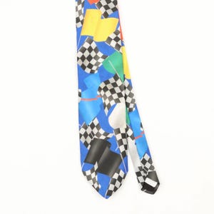 May include: A blue necktie featuring a repeating pattern of black and white chequered racing flags, solid yellow flags, and solid black flags. The design includes thin red and white lines scattered across the vibrant blue background fabric.