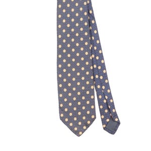 May include: A necktie in a dark blue hue featuring a repeating pattern of small, light yellow floral motifs. The fabric displays a subtle, intricate geometric texture throughout the background, with a pointed tip and a visible label on the back.