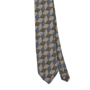 Può includere: Una cravatta con un motivo geometrico ripetuto di cubi nei toni del blu, grigio scuro e beige. Il tessuto ha un aspetto strutturato e una piccola etichetta nera sul retro dell'estremità stretta riporta la scritta 100% SILK.