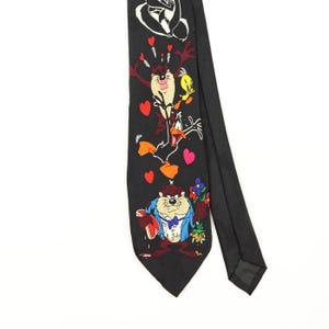 May include: A black necktie featuring a colourful graphic print of Looney Tunes characters including the Tasmanian Devil, Tweety Bird, and Daffy Duck, accented with red heart shapes and a bouquet of flowers held by the Tasmanian Devil character.