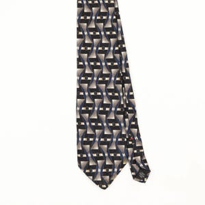 May include: A necktie featuring a repeating geometric pattern of black, silver, and dark blue shapes. The design consists of alternating trapezoidal forms and small circles arranged in a grid. A small black label is visible on the back.