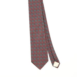 Könnte beinhalten: Eine Krawatte mit einem sich wiederholenden geometrischen Muster in Dunkelrot, Petrol und Schwarz. Das Design besteht aus kleinen, miteinander verbundenen Formen, die in einem dichten, gleichmäßigen Raster auf der Stoffoberfläche angeordnet sind.
