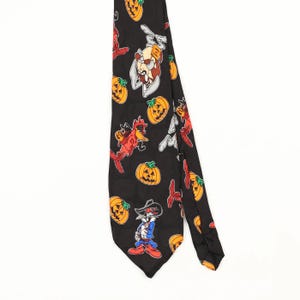 Könnte beinhalten: Eine schwarze Krawatte mit einem sich wiederholenden Muster aus orangefarbenen Kürbissen und verschiedenen Looney Tunes-Zeichentrickfiguren, darunter Bugs Bunny und der Tasmanische Teufel, in leuchtenden Farben auf dem Stoff.