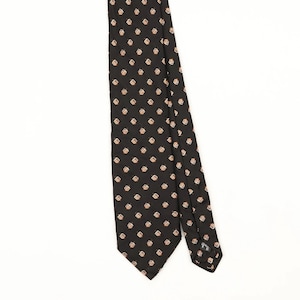 May include: A black necktie featuring a repeating pattern of small, light-coloured dreidel icons arranged in a grid. The tie has a pointed end and a visible label on the back of the narrow tail, showcasing a consistent geometric design throughout.