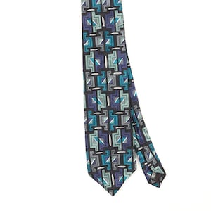 May include: A necktie featuring a repeating geometric pattern of interlocking shapes in shades of teal, dark blue, grey, and white on a black background. The design consists of stylised rectangular and angular motifs arranged in vertical columns.
