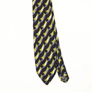 Peut inclure: Une cravate présentant un motif géométrique répétitif composé de formes courbes noires, vert citron et bleues. Le tissu a une texture lisse et une extrémité pointue. Une petite étiquette rectangulaire est fixée au dos près de la pointe.