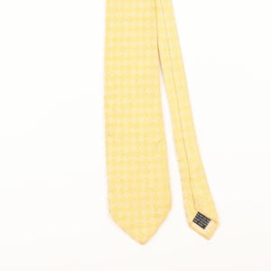 May include: A yellow tie with a subtle, repeating pattern. The tie is angled across a white background, showcasing its texture and design. The tie's color is a soft, pale yellow, and the pattern appears to be a series of small, repeating shapes.