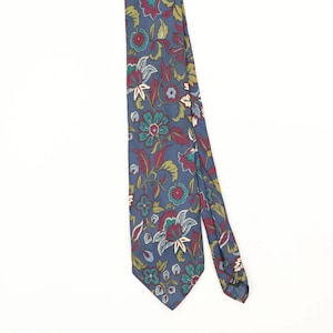 May include: A necktie featuring a blue background with a repeating floral pattern in shades of red, teal, light blue, and cream. The design consists of stylized flowers and leaves arranged across the fabric, with a pointed tip at the bottom end.