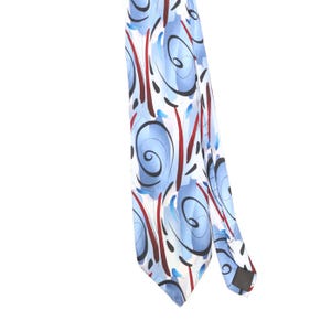 May include: A necktie featuring a white background with a repeating pattern of light blue circular brushstrokes, dark red vertical lines, and thin black swirling accents. The tie has a pointed tip and a smooth fabric finish with a visible inner lining.