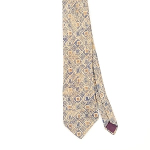 Peut inclure: Une cravate présentant un motif répétitif de losanges dans des tons de beige, de brun clair et de bleu sourd. Le design se compose de petits carrés à l'intérieur de losanges, avec une doublure violet foncé visible sur le pan replié de la cravate.
