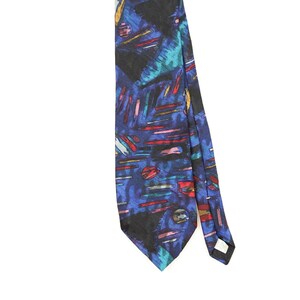May include: A necktie featuring a deep blue background with an abstract pattern of black, red, teal, and yellow brushstroke-like lines and circular shapes. The fabric has a smooth texture, and a small white care label is visible on the back.