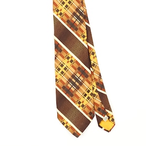 Puede incluir: Una corbata con un patrón de cuadros diagonal en tonos marrón, amarillo y naranja. El diseño incluye bandas texturizadas de color marrón sólido alternadas con secciones de líneas que se cruzan, con una pequeña etiqueta blanca visible.