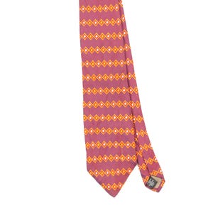 Pode incluir: Uma gravata na cor rosa empoeirado com um padrão geométrico repetitivo de diamantes laranja e brancos dispostos em linhas horizontais. A gravata inclui uma pequena etiqueta preta na parte de trás que diz Imported Silk Made in U.S.A.
