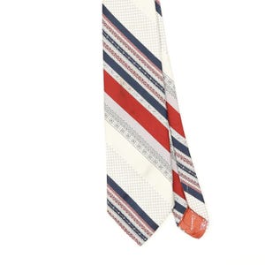 Peut inclure: Une cravate présentant un motif à rayures diagonales crème, bleu marine et rouge. Le design comprend des sections avec une texture à petits points, des bandes de couleur unie et des bordures décoratives complexes aux formes géométriques.
