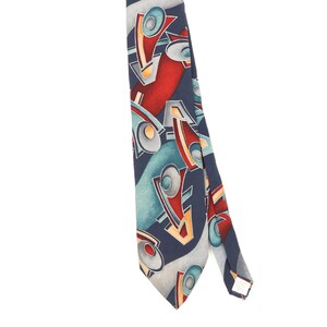 Può includere: Una cravatta con sfondo blu scuro e un motivo ripetitivo di forme geometriche astratte in rosso, verde acqua, azzurro e giallo. Il design include linee curve ed elementi circolari disposti in una composizione a strati sovrapposti.