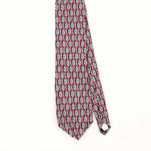 Puede incluir: Una corbata con un patrón geométrico repetitivo de diamantes gris oscuro delineados en blanco, con acentos granates y verde azulado dentro de cada forma. La corbata tiene un extremo puntiagudo y una pequeña etiqueta de tela blanca al dorso.