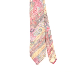 May include: A necktie featuring a complex, multi-coloured paisley pattern in shades of pink, yellow, and muted grey. The design consists of swirling organic shapes and diagonal stripes that run across the fabric, creating a textured visual effect.