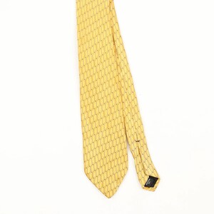 Peut inclure: Une cravate jaune avec un motif géométrique en nid d'abeille noir répétitif. La cravate présente une extrémité pointue et une étiquette noire au dos indiquant Imported Silk. Le tissu a une texture lisse et un motif uniforme sur toute la surface.