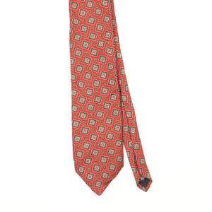 Peut inclure: Une cravate rouge ornée d'un motif géométrique répétitif composé de petits carrés aux accents bleus, jaunes et blancs. La cravate présente une extrémité pointue et une étiquette en tissu noir fixée au dos, offrant un design structuré.