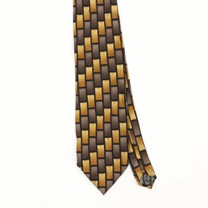 Peut inclure: Une cravate avec un motif géométrique répétitif composé de rectangles marron foncé et de rectangles jaune doré avec des détails de lignes verticales. L'étiquette au dos indique 100% SILK et MADE IN KOREA.