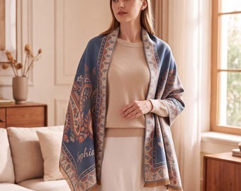 May include: A blue shawl featuring a detailed paisley pattern in shades of orange, cream, and brown. The shawl has a decorative border with a repeating leaf motif and the name Sophia printed in a cursive script on the lower front section.