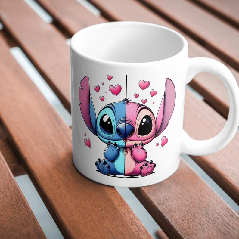 May include: A white ceramic mug featuring a split-color graphic of a cartoon creature. The left side is blue and the right side is pink, separated by a vertical line. The character is surrounded by small pink hearts floating in the air.