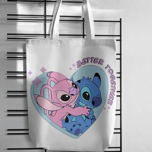 May include: A white tote bag featuring a graphic print of a pink character and a blue character hugging inside a light blue heart shape. The text "BETTER TOGETHER" is printed in purple letters along the right side of the heart, accompanied by small purple star icons.