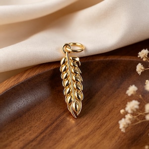 Peut inclure: Un pendentif doré poli en forme d'épi de blé, doté d'une tige centrale avec plusieurs segments de grains arrondis et d'un petit anneau circulaire fixé au sommet pour la suspension, présentant une finition métallique lisse et réfléchissante.