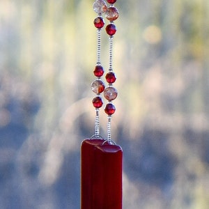 Handmade wind chime made with Red Ruby Moss Crystal stones flanked by Austrian crystal beads, anchored by two pieces of red fused glass, hanging from tree