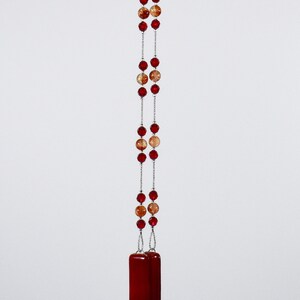 Puede incluir: Un collar largo con cuentas rojas y naranjas y un colgante rectangular rojo.