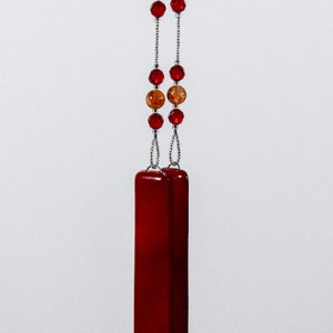Puede incluir: Un collar con un colgante de vidrio rojo, una cadena de plata y cuentas rojas y marrones.