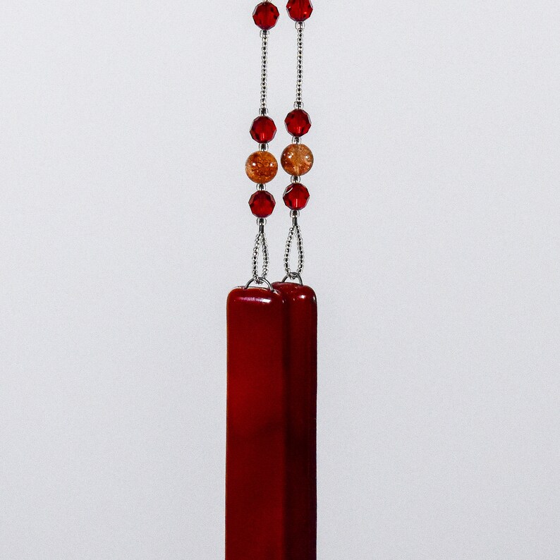 Puede incluir: Un collar con un colgante de vidrio rojo, una cadena de plata y cuentas rojas y marrones.