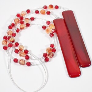 Puede incluir: Un collar largo con cuentas rojas y naranjas y dos colgantes de vidrio rojo.