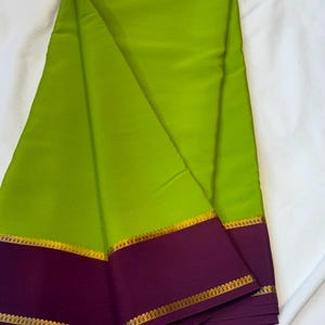 May include: A vibrant lime green fabric featuring a wide, deep purple border along the bottom edge. The purple border is accented with a thin, metallic gold woven trim that runs horizontally across the fabric, creating a distinct contrast.
