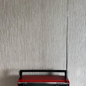 Könnte beinhalten: Ein tragbares Vintage-Radio vom Typ VEF 202 mit einem leuchtend roten Gehäuse, einem schwarzen Tragegriff und einer langen, dünnen, silbernen Teleskopantenne. Die Frontplatte zeigt eine grüne Frequenzanzeige, ein Lautsprechergitter mit silbernen Stäben.