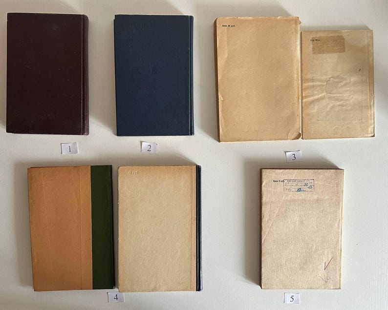 K&ouml;nnte beinhalten: Eine Sammlung von sieben rechteckigen B&uuml;chern, die in zwei Reihen angeordnet sind. Die B&uuml;cher haben verschiedene einfarbige Einb&auml;nde in Dunkelbraun, Marineblau und Beige. Einige Einb&auml;nde weisen Gebrauchsspuren, Papieretiketten und Stempel auf.