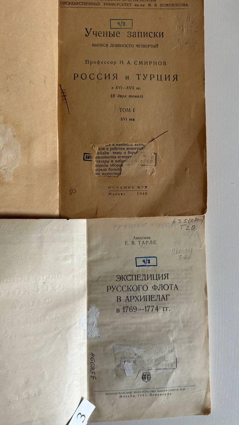 K&ouml;nnte beinhalten: Zwei alte Buchumschl&auml;ge aus Papier in Beige und Off-White mit schwarzem kyrillischem Text. Der obere Umschlag tr&auml;gt den Titel "Россия и Турция" und das Datum 1946. Der untere Umschlag zeigt den Titel "Экспедиция русского флота в архипелаг" und das Jahr 1945.