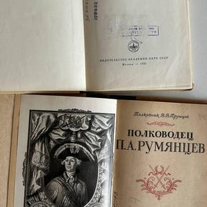 K&ouml;nnte beinhalten: Zwei aufgeschlagene alte B&uuml;cher mit cremefarbenen Seiten und schwarzem kyrillischem Text. Der Titel des oberen Buches enth&auml;lt "ФЕЛЬДМАРШАЛ РУМЯНЦЕВ". Das untere Buch zeigt ein schwarz-wei&szlig;es Portr&auml;t von P.A. Rumjanzew und den Titel "ПОЛКОВОДЕЦ П.А.РУМЯНЦЕВ".