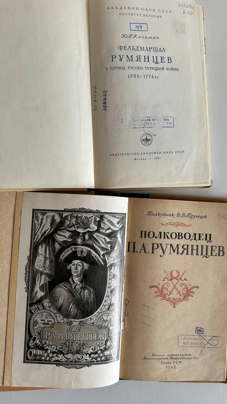 K&ouml;nnte beinhalten: Zwei aufgeschlagene alte B&uuml;cher mit cremefarbenen Seiten und schwarzem kyrillischem Text. Der Titel des oberen Buches enth&auml;lt "ФЕЛЬДМАРШАЛ РУМЯНЦЕВ". Das untere Buch zeigt ein schwarz-wei&szlig;es Portr&auml;t von P.A. Rumjanzew und den Titel "ПОЛКОВОДЕЦ П.А.РУМЯНЦЕВ".