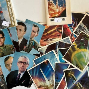 Puede incluir: Una colección de postales y folletos vintage con temática espacial. Las postales presentan retratos de cosmonautas e ilustraciones de cohetes, satélites y escenas de exploración espacial. Los folletos tienen texto en ruso.