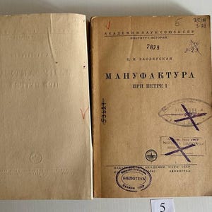 K&ouml;nnte beinhalten: Ein aufgeschlagenes antikes Buch mit beigen Seiten. Die rechte Seite zeigt kyrillischen Text, darunter den Titel "МАНУФАКТУРА ПРИ ПЕТРЕ I", handschriftliche Zahlen und mehrere violette Stempel mit durchgestrichenen Markierungen. Die linke Seite ist leer mit einem Logo.