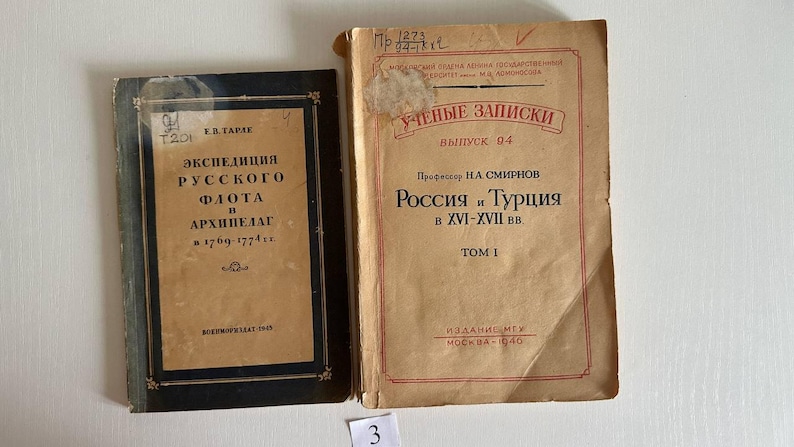 K&ouml;nnte beinhalten: Zwei alte B&uuml;cher mit gealterten Papierumschl&auml;gen. Das linke Buch hat einen schwarzen Rand und kyrillischen Text, darunter 'ЭКСПЕДИЦИЯ РУССКОГО ФЛОТА В АРХИПЕЛАГ'. Das rechte Buch ist hellbraun mit roten R&auml;ndern und kyrillischem Text, darunter 'РОССИЯ И ТУРЦИЯ В XVI-XVII ВВ'.
