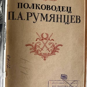 K&ouml;nnte beinhalten: Eine Buch-Titelseite auf beigem Papier mit dem russischen Text "Полковник В.В.Прунцов", "ПОЛКОВОДЕЦ П.А.РУМЯНЦЕВ" und "1946". Ein rotes dekoratives Emblem mit gekreuzten Schwertern und einem Lorbeerkranz befindet sich &uuml;ber einem blauen Bibliotheksstempel.