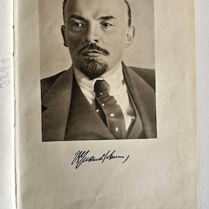 K&ouml;nnte beinhalten: Ein schwarz-wei&szlig;es Portr&auml;t von Wladimir Lenin, das auf eine Buchseite gedruckt ist. Das Bild zeigt einen Mann mit Spitzbart und Schnurrbart in Anzug und Krawatte. Unter dem Portr&auml;t befindet sich eine Unterschrift in schwarzer Tinte. Ein kleines wei&szlig;es Etikett mit der Zahl 1 ist zu sehen.