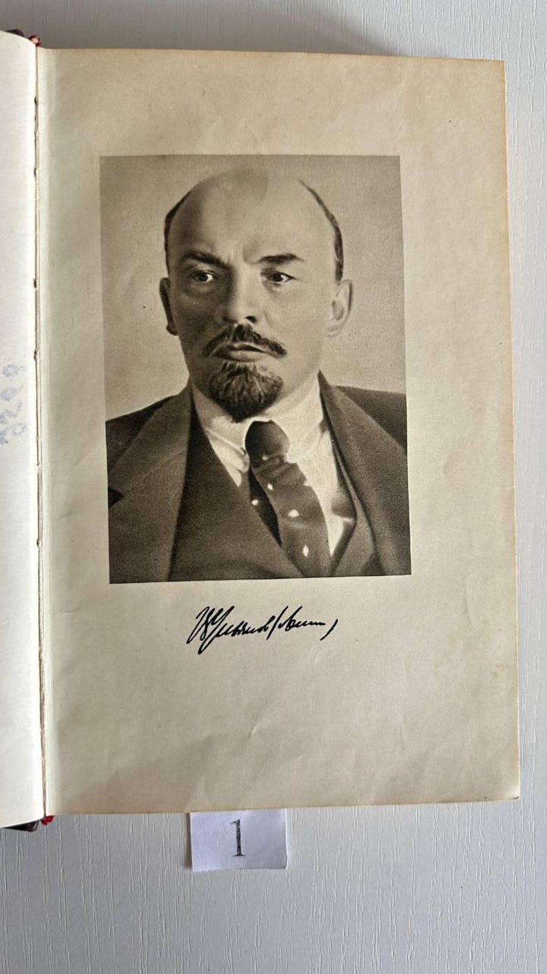 K&ouml;nnte beinhalten: Ein schwarz-wei&szlig;es Portr&auml;t von Wladimir Lenin, das auf eine Buchseite gedruckt ist. Das Bild zeigt einen Mann mit Spitzbart und Schnurrbart in Anzug und Krawatte. Unter dem Portr&auml;t befindet sich eine Unterschrift in schwarzer Tinte. Ein kleines wei&szlig;es Etikett mit der Zahl 1 ist zu sehen.