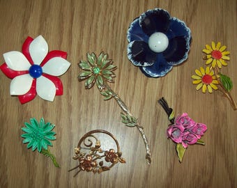 May include: A collection of vintage flower brooches in various colors, including red, white, blue, green, yellow, and pink. The brooches are made of metal and enamel, and feature different floral designs.